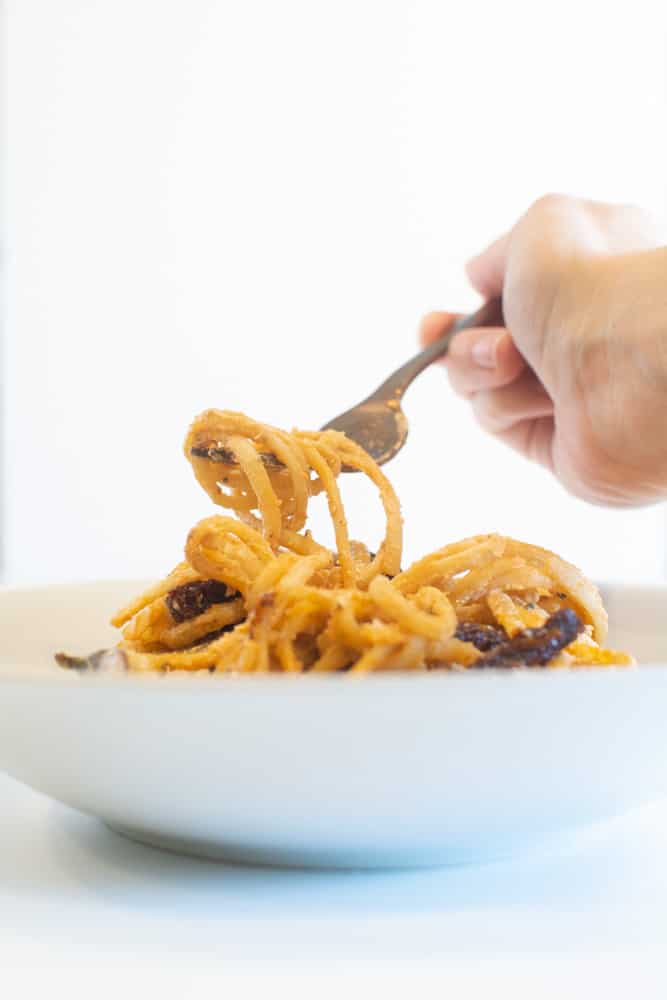 hand holding fork and twirling pasta out of bowl