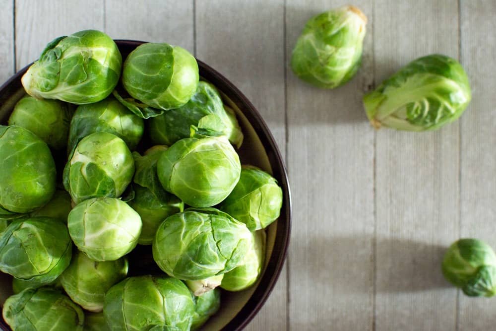 Bowl of raw Brussels on light wood background