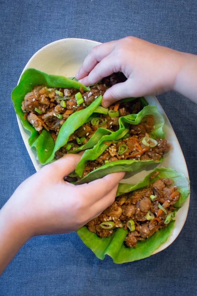 Hands grabbing lettuce wraps off of serving platter