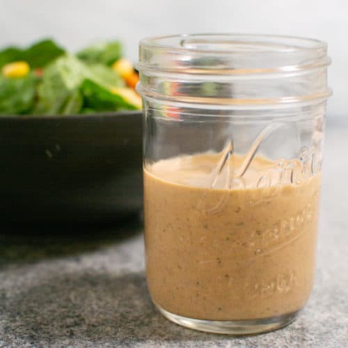 small mason jar full of dressing with a bowl of salad in the background