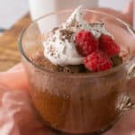 chocolate cake in see through glass mug with whipped cream and raspberries on top