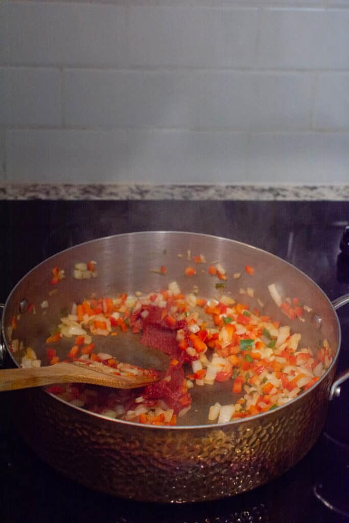 adding tomato paste to sautéed vegetables
