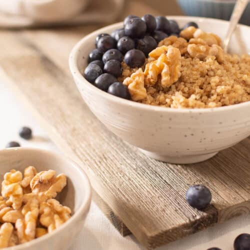 Quinoa porridge in bowl topped with fresh blueberries and walnuts