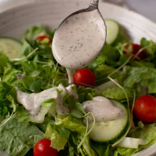 vertical of salad with spoonful of ranch being poured on