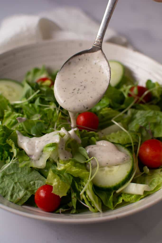vertical of salad with spoonful of ranch being poured on
