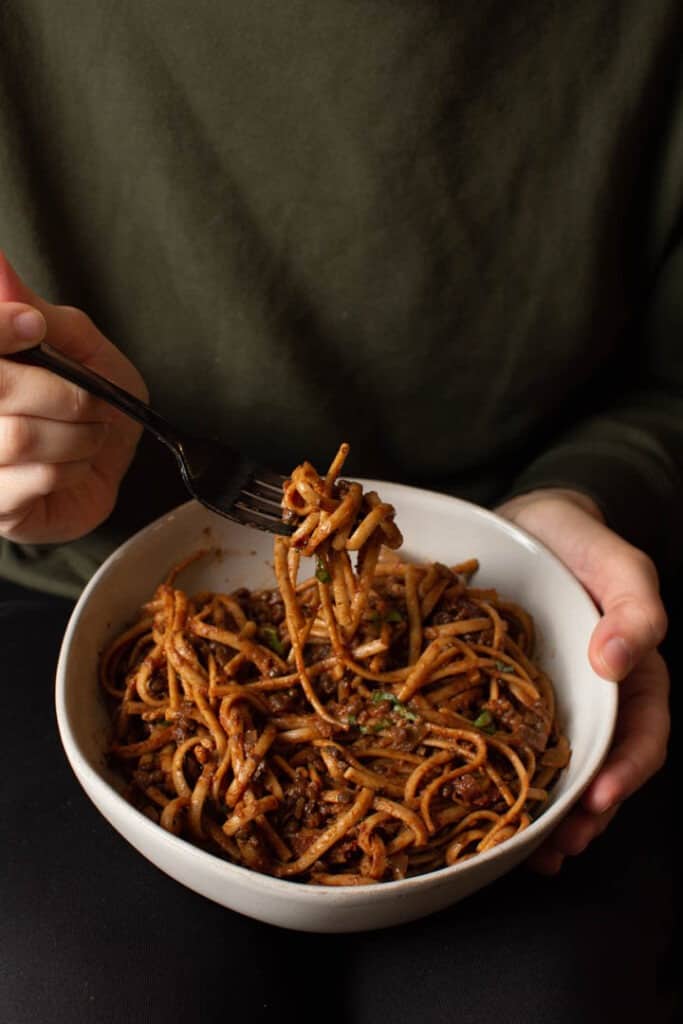 holding a bowl of pasta with some on a fork