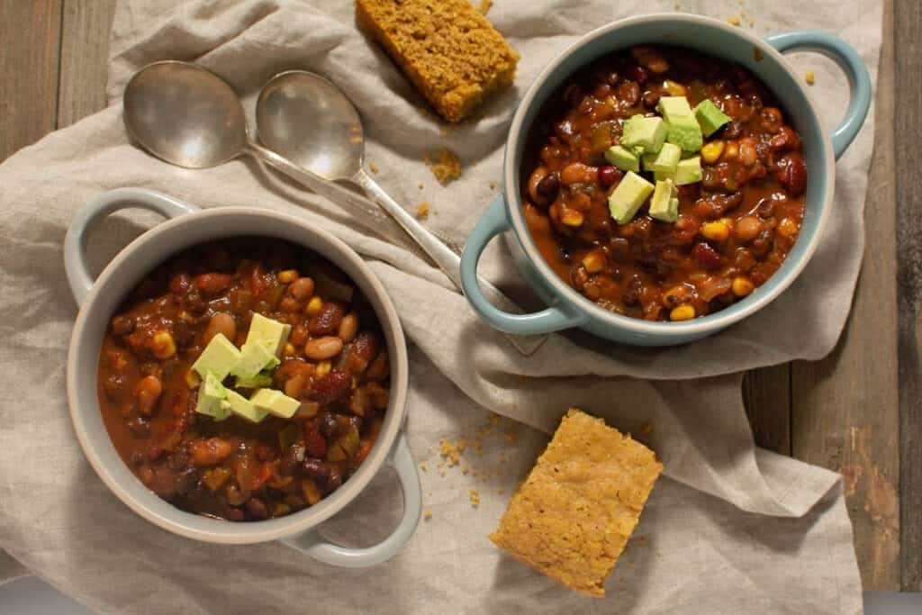 Birdseye view of two bowls of chili topped with avocado and a side of cornbread.