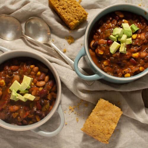 Birdseye view of two bowls of chili topped with avocado and a side of cornbread.