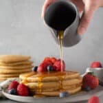 Hand pouring syrup on top of pancakes