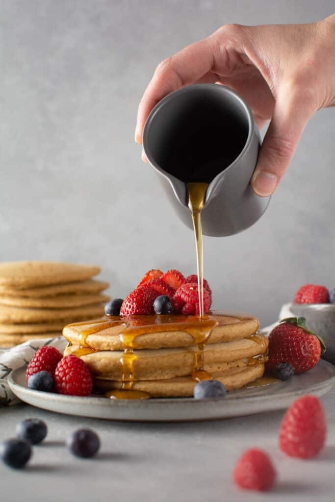 Hand pouring syrup on top of pancakes