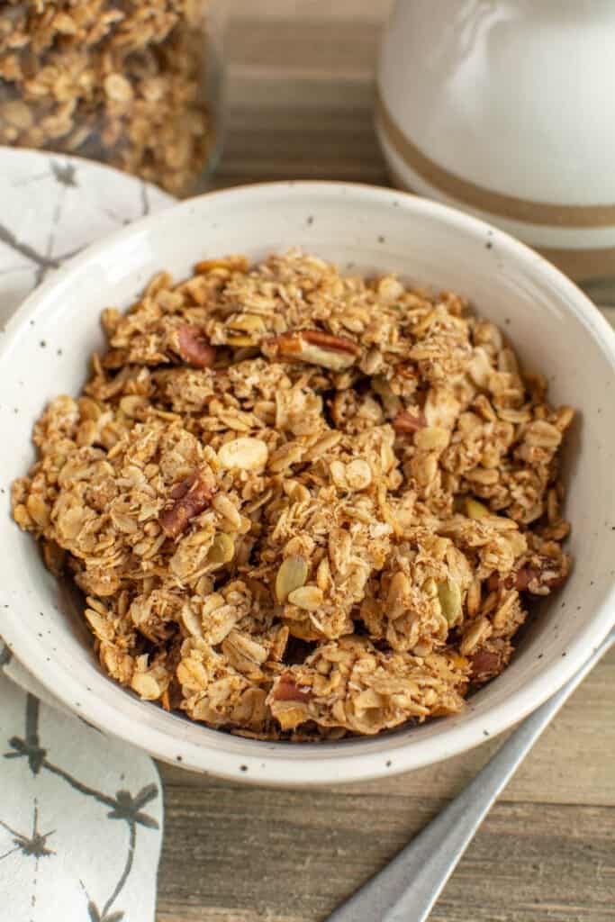 Bowl of granola next to container full of granola and jug of milk