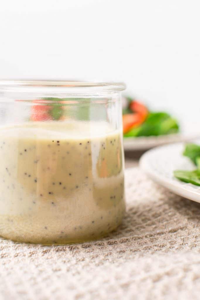 Glass container of dressing in front of plates of salad