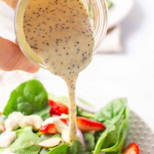 Pouring dressing over a green salad with strawberries
