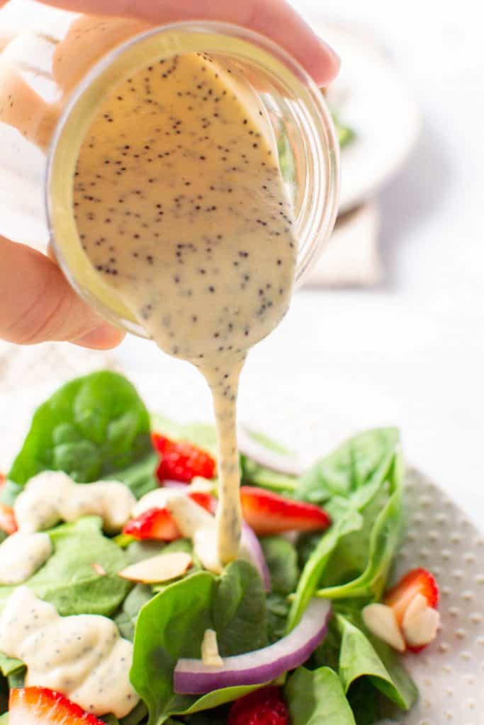 Pouring dressing over a green salad with strawberries