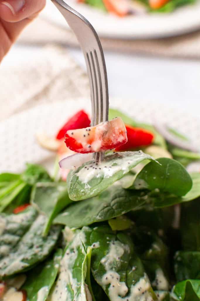 A forkful of spinach, strawberry, and onion salad with poppy seed dressing