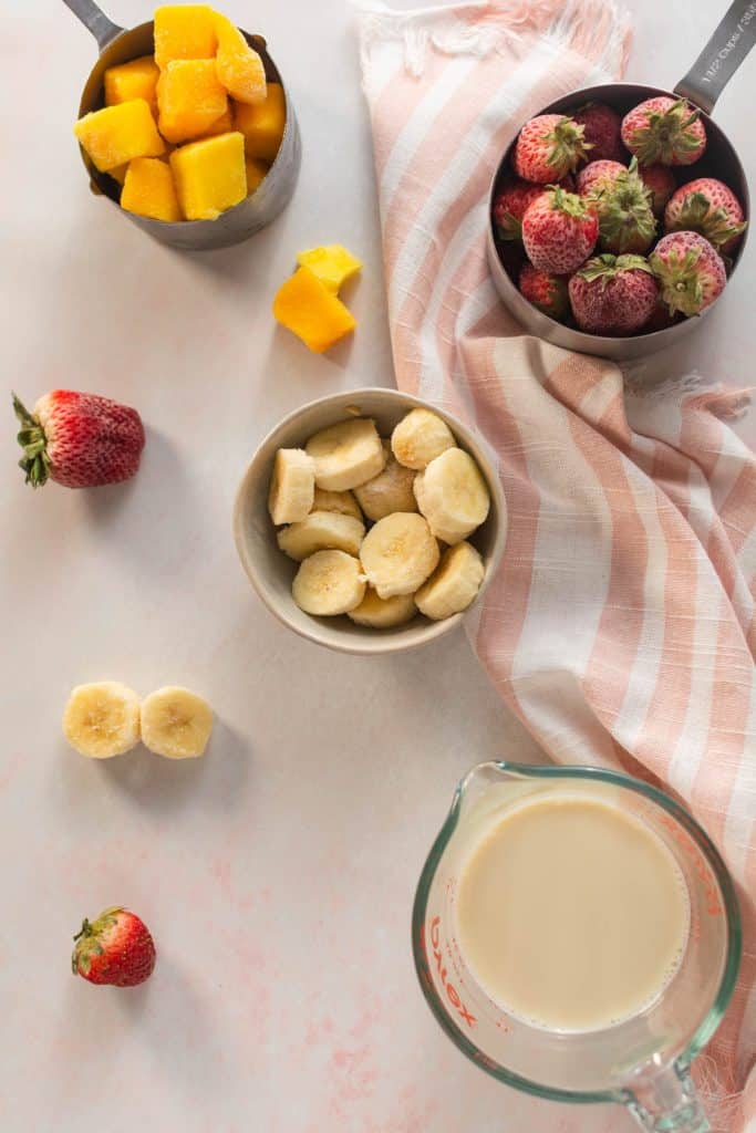 Overhead shot of ingredients needed to make a strawberry mango smoothie bowl.