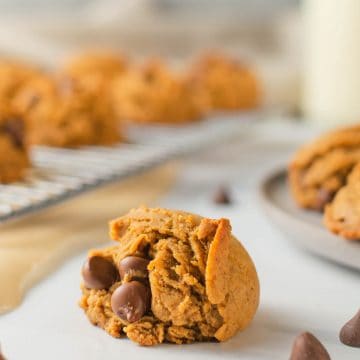 Close up of cookie with milk and drying rack of cookies in the background.