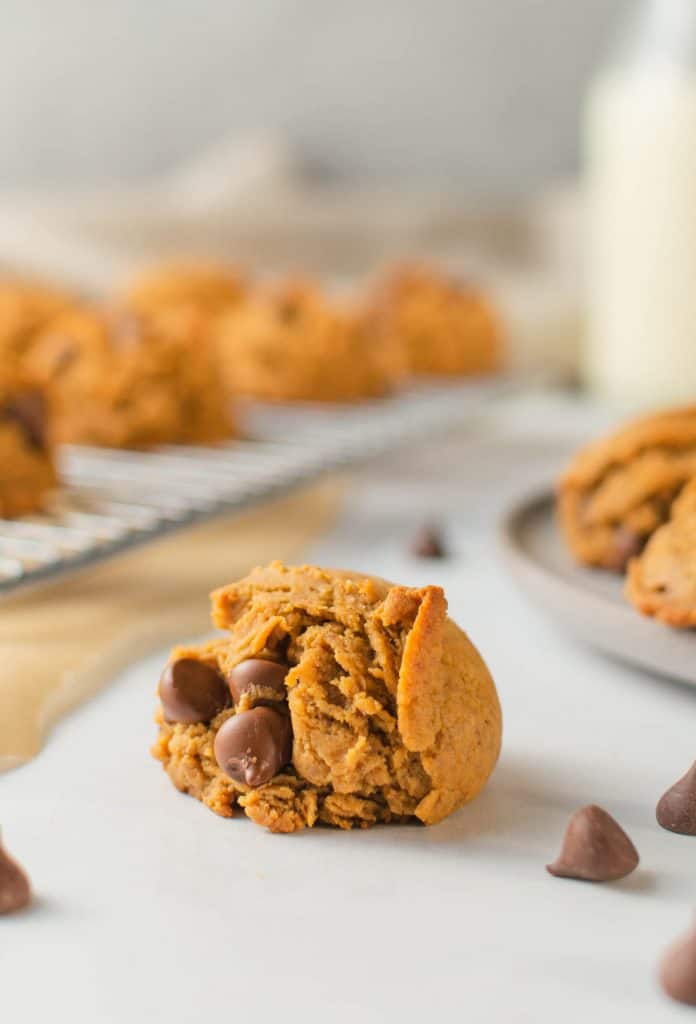 Close up of cookie with milk and drying rack of cookies in the background.