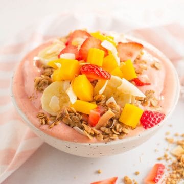 Smoothie bowl topped with granola and fruit in a speckled bowl.