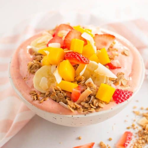 Smoothie bowl topped with granola and fruit in a speckled bowl.