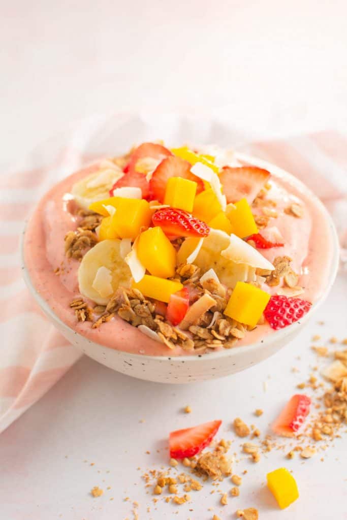 Smoothie bowl topped with granola and fruit in a speckled bowl.