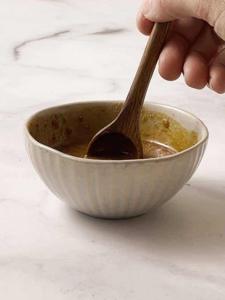 someone stirring a small bowl of peanut sauce.