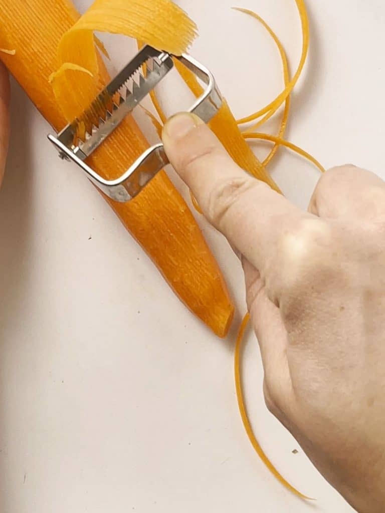 someone using a julienne peeler on a carrot.