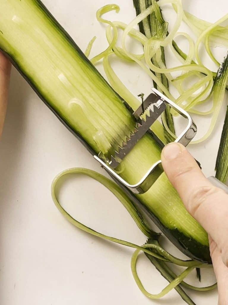 picture of someone using a julienne peeler on a cucumber