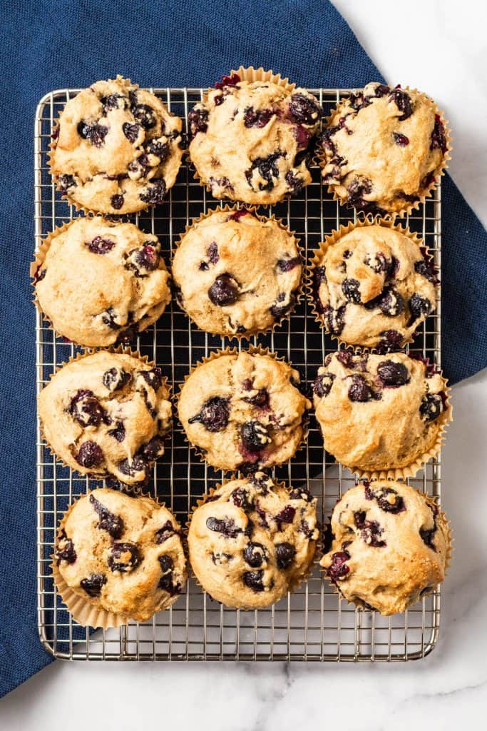 Overhead shot of 12 muffins on a cooling rack on a blue napkin.