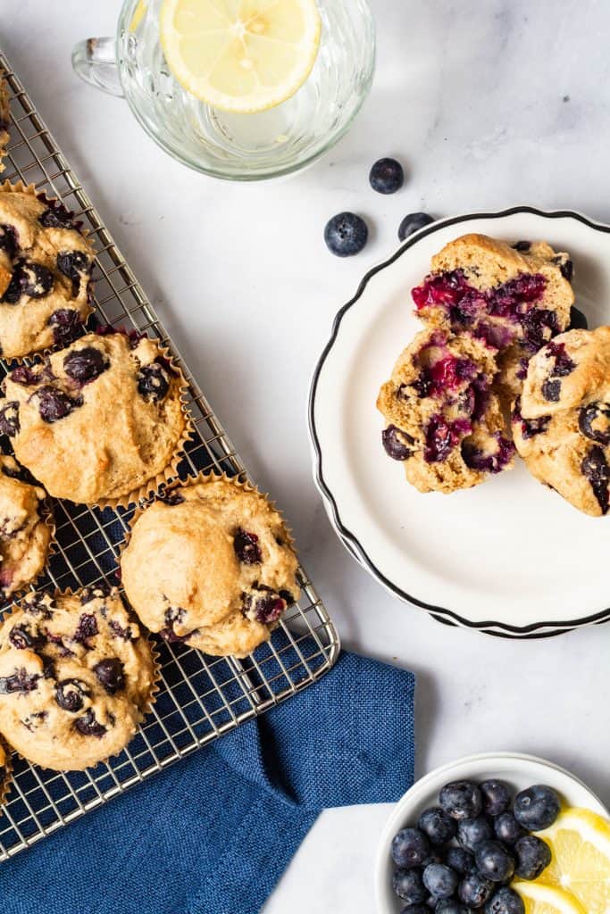 Overhead of two muffins on a white plate with one cut in half and a glass and cooling rack in the scene.