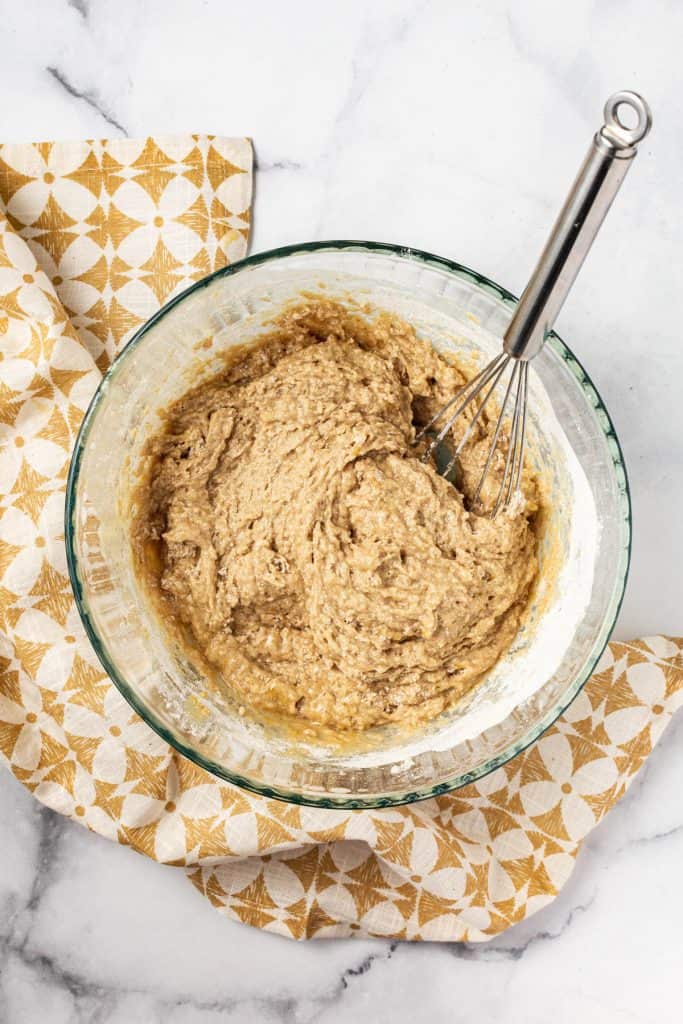 Wet and dry ingredients stirred together in a glass bowl with yellow napkin.