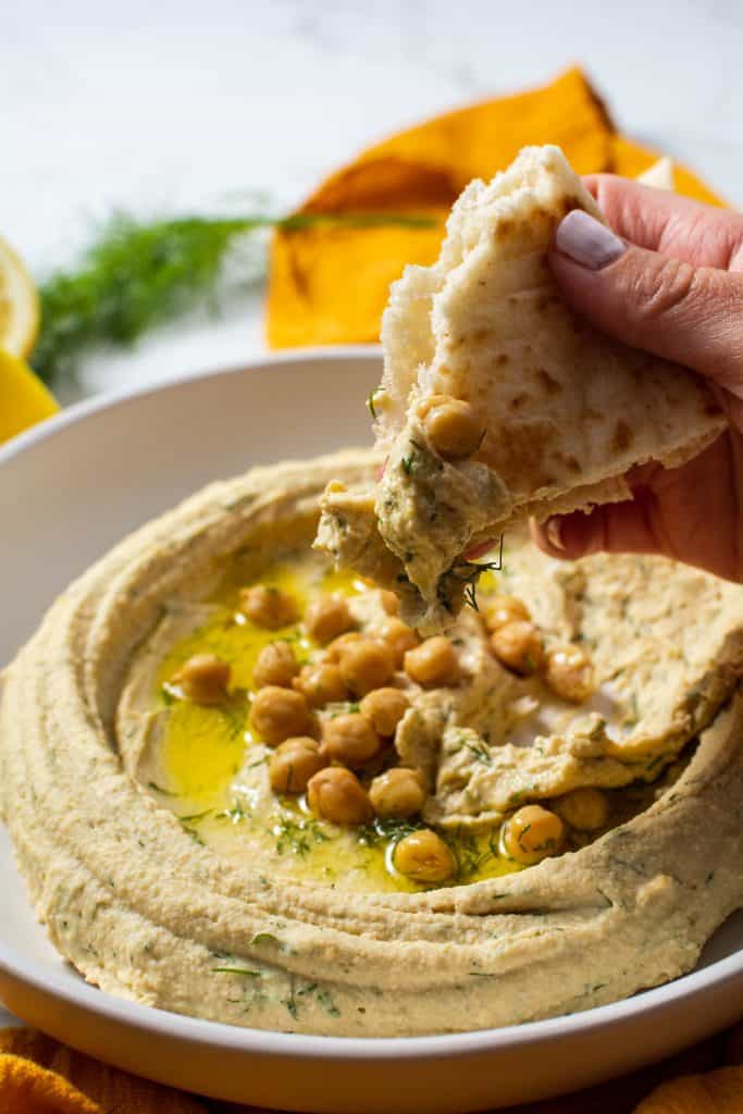Closeup of someone dipping their pita bread into the hummus.