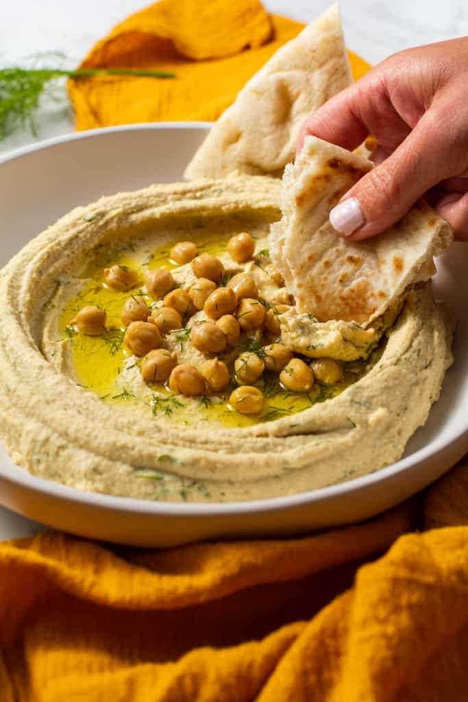 Close up of hummus and someone dipping the pita bread.