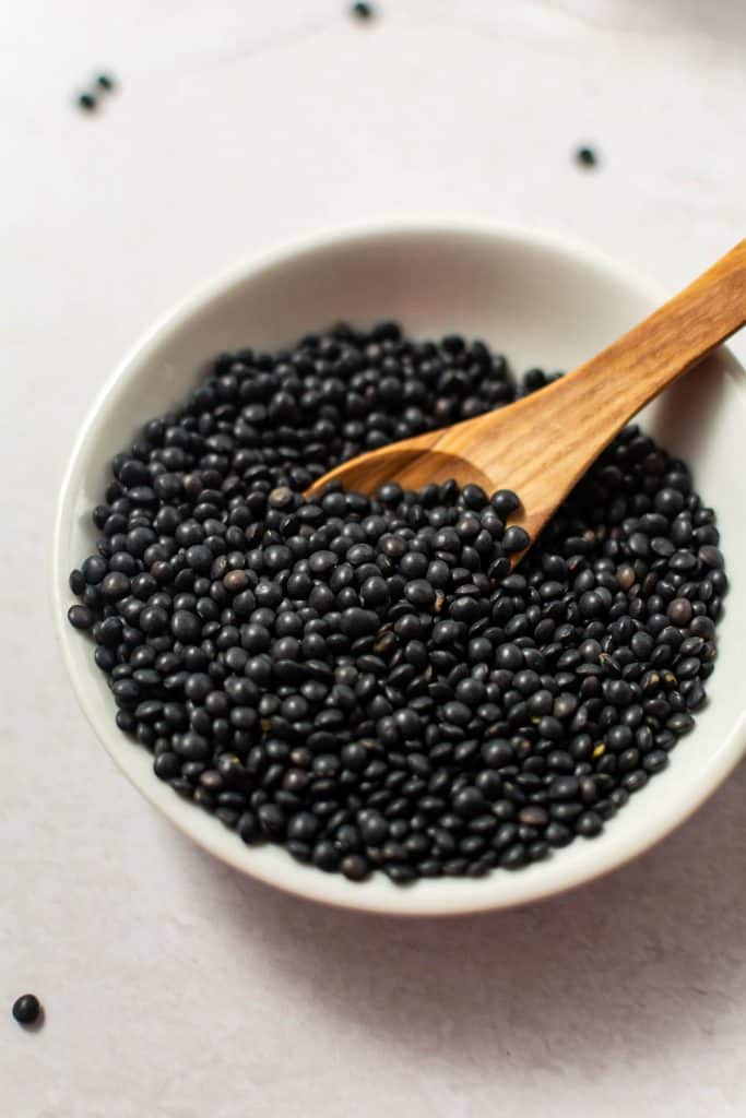 Small bowl with dry black lentils and wooden spoon.