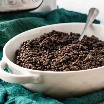 White serving bowl with black lentils and instant pot in the background.