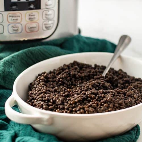 White serving bowl with black lentils and instant pot in the background.