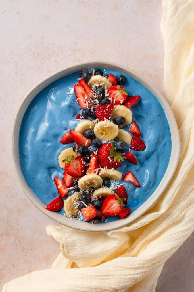 Birdseye view of smoothie bowl with toppings and white towel.