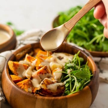 hand pouring dressing over sweet potato hash with a wooden spoon.