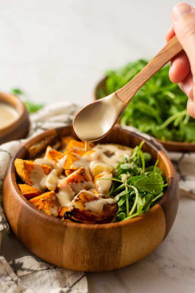 hand pouring dressing over sweet potato hash with a wooden spoon.