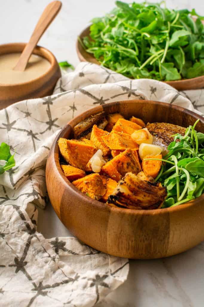 wooden bowl with hash with a plate of arugula and bowl of dressing in the back.