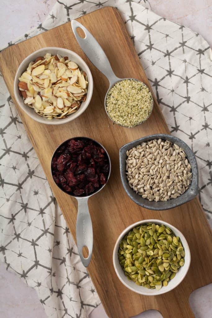 Wood serving board with bowls full of nuts and seeds for mix.