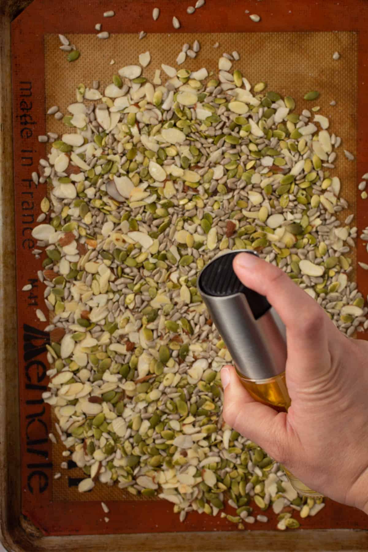 hand spraying oil onto seeds on cookie tray.