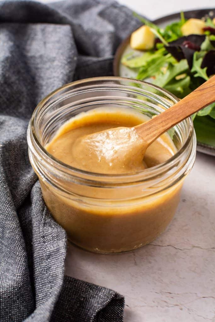 Glass jar with dressing and wooden spoon and salad in the corner.