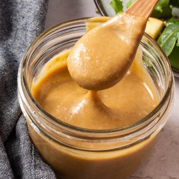 Wooden spoon dipping dressing out of glass container.