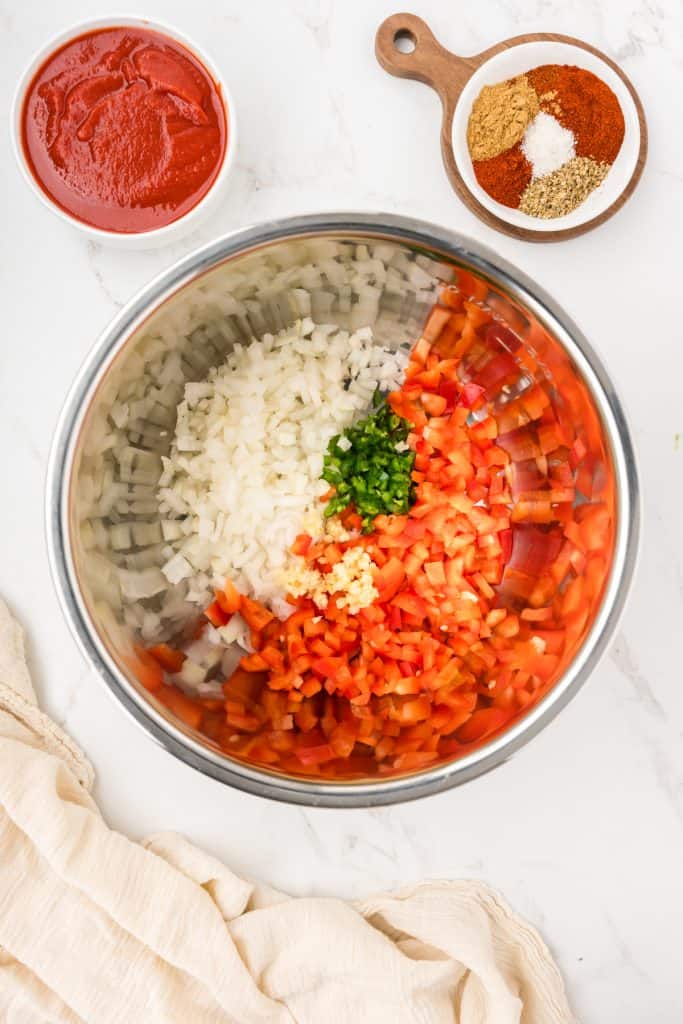 Overhead image of onion, red bell pepper, jalapeno and garlic in the insert of an instant pot.