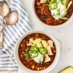 Overhead shot of two bowls of chili topped with chips, avocado, and sour cream.