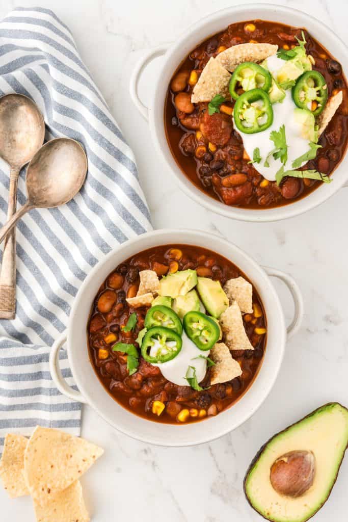 Overhead shot of two bowls of chili topped with chips, avocado, and sour cream.