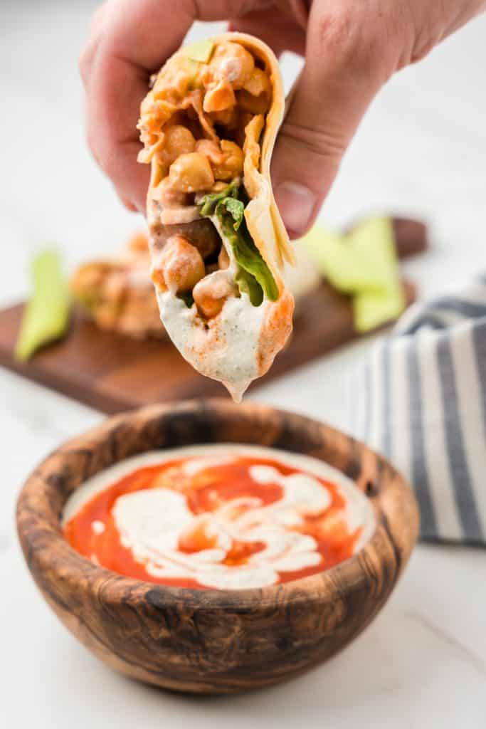Side view of a hand holding half of a wrap dipped in a sauce made from ranch and hot sauce.
