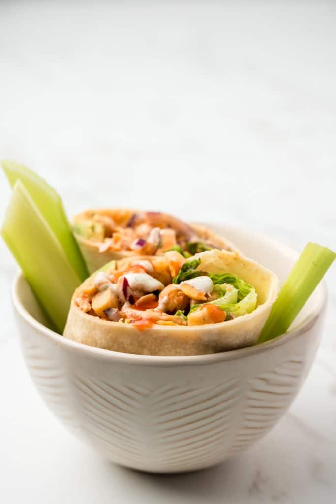 Side view of chickpea wrap halves in a bowl with a couple pieces of celery.