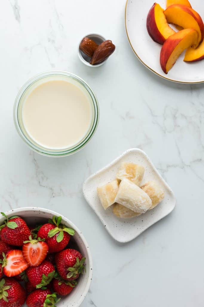 Overhead shot of ingredients: sliced peaches, dates, frozen banana, soy milk, and strawberries.